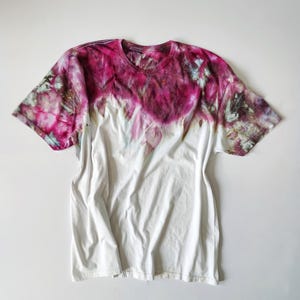 Puede incluir: Camiseta blanca con dise&ntilde;o tie-dye. La parte superior de la camiseta est&aacute; te&ntilde;ida en tonos rosas y morados, que se funden en blanco. Tiene cuello redondo y mangas cortas, y est&aacute; colocada plana sobre un fondo blanco.