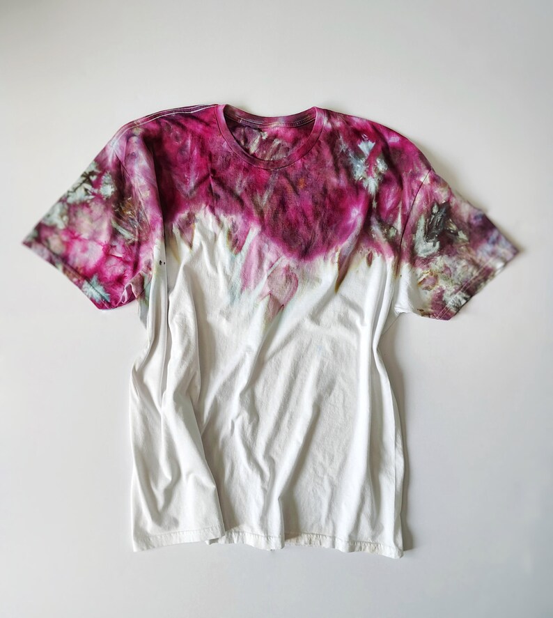 Puede incluir: Camiseta blanca con dise&ntilde;o tie-dye. La parte superior de la camiseta est&aacute; te&ntilde;ida en tonos rosas y morados, que se funden en blanco. Tiene cuello redondo y mangas cortas, y est&aacute; colocada plana sobre un fondo blanco.