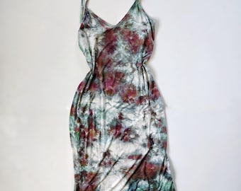 May include: A tie-dye slip dress with thin spaghetti straps. The dress features a V-neck and a knee-length hemline. The fabric is a blend of white, burgundy, teal, and green hues, creating a unique, artistic pattern. The dress is laid flat on a white surface.