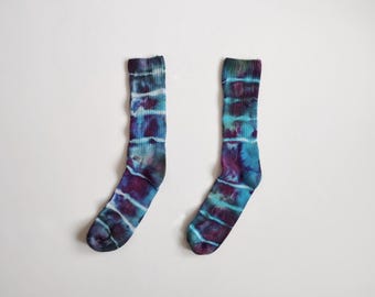 May include: A pair of tie-dye socks in shades of blue, purple, and teal. The socks have a striped pattern and are made of a soft, comfortable material. The socks are a unique and stylish accessory.