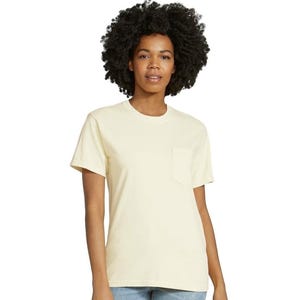 Op de afbeelding: Een lichtgeel t-shirt met een borstzak. De korte mouwen shirt is gemaakt van een zacht materiaal en wordt gedragen door een persoon met donker krullend haar en een spijkerbroek.