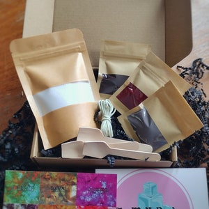 May include: A craft kit with various colored dye packets, wooden spoons, and a card with color swatches. The kit includes a box, several small bags of dye, and a card with the text "EyeMeUpDesigns".
