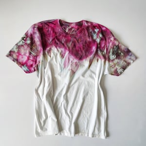 Puede incluir: Camiseta blanca con dise&ntilde;o tie-dye. La parte superior de la camiseta est&aacute; te&ntilde;ida en tonos rosas y morados, pasando a blanco. La camiseta tiene mangas cortas y cuello redondo.