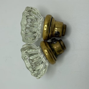 May include: Two antique glass door knobs with brass bases. The glass is clear and has a faceted design. The brass bases have a gold finish.