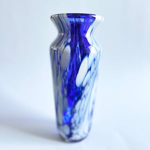 Può includere: Un vaso di vetro blu e bianco con un motivo a spirale. Il vaso è fatto di vetro trasparente con vortici blu e bianchi.
