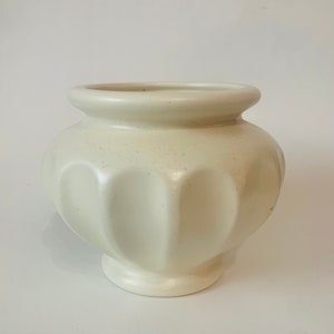 May include: A white ceramic planter with a fluted design. The planter has a rounded body and a wide, flat base.