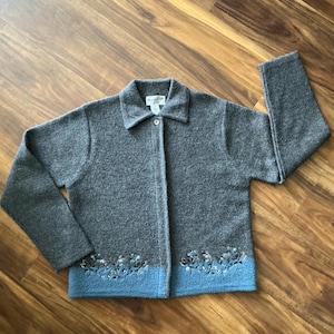 Puede incluir: Chaqueta de lana gris con cuello y cierre de botones. La chaqueta presenta un dobladillo azul claro con bordado floral. La etiqueta Pendleton es visible en el cuello.