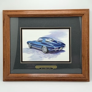 May include: Framed print of a blue 1963 Corvette Split Window Coupe. The artwork is set against a black mat and framed in a brown wooden frame. The print includes the text "American Memory Prints".