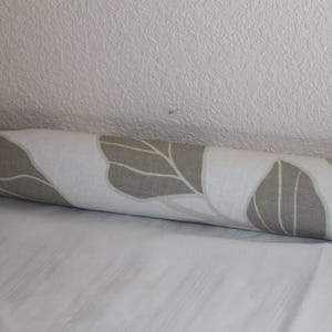 May include: A white and beige patterned bolster pillow with a floral design.