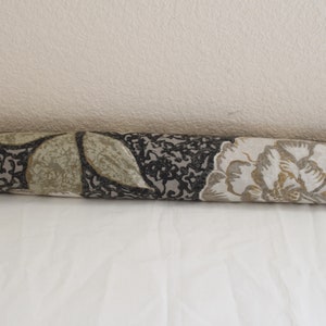 May include: A brown, beige, and white floral patterned doorstop. The doorstop is a cylinder shape.