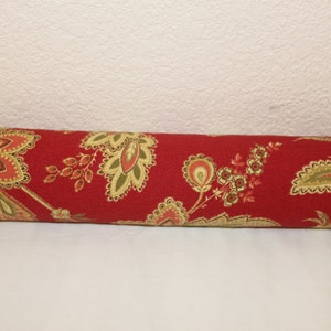 May include: A cylindrical decorative door draft stopper with a red floral pattern. The fabric features large, stylized flowers in shades of gold, green, and red. The stopper is designed to block drafts and add a decorative touch to a room.