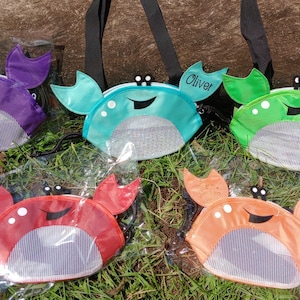 May include: Five colorful crab-shaped mesh bags with adjustable straps. The bags are purple, teal, green, red, and orange. The bags have a mesh front and a solid back. The bags are personalized with the names "Oliver" and "Emily".
