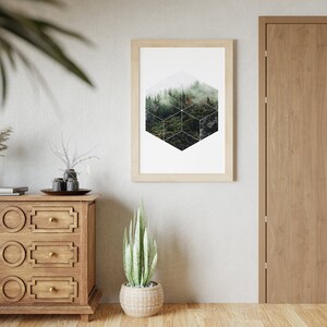 May include: A framed print with a geometric forest design hangs on a light grey wall. A wooden chest of drawers and a potted snake plant are in the foreground. A wooden door is on the right.