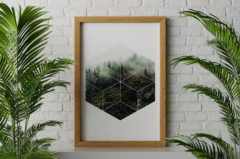May include: A framed art print depicting a forest scene within a geometric design. The artwork is set against a white background and framed in a light brown wooden frame. Green plants frame the artwork.