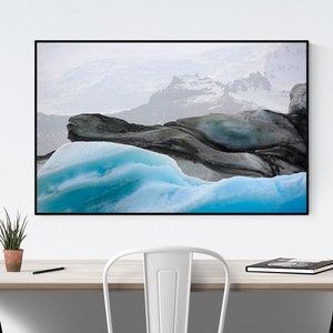 Op de afbeelding: Een ingelijste landschapsfoto met een gletsjer. De afbeelding toont levendige turquoise ijsformaties op de voorgrond, die contrasteren met donkere, getextureerde rotsformaties. Op de achtergrond zijn besneeuwde bergen te zien. De lijst is zwart.
