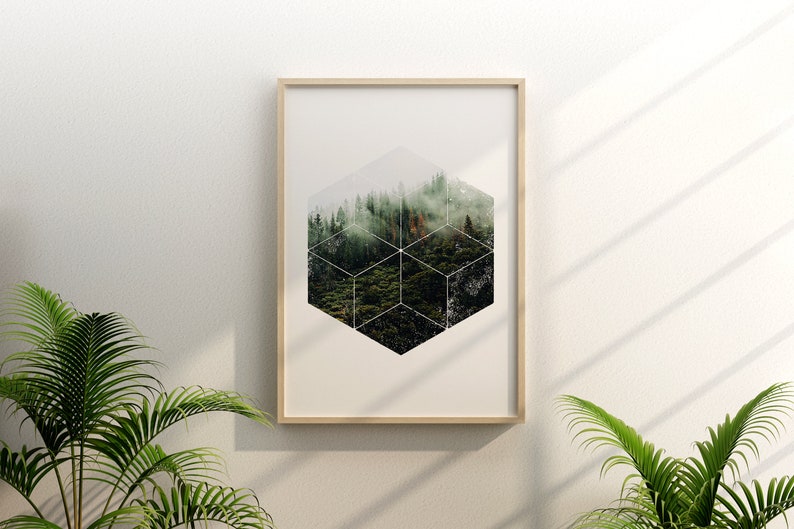 May include: A framed art print with a geometric forest design. The artwork depicts a forest landscape within a cube-like structure, set in a light wood frame. The print is displayed on a white wall, with green plants in the foreground.
