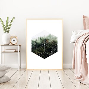 May include: A framed art print with a geometric forest design. The artwork is in a gold frame, displayed in a bedroom. A white bed with pink accents and a side table with a vase and clock are also visible. The room has wooden flooring.