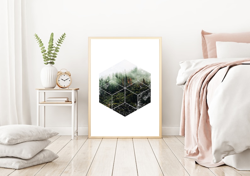 May include: A framed art print with a geometric forest design. The artwork is in a gold frame, displayed in a bedroom. A white bed with pink accents and a side table with a vase and clock are also visible. The room has wooden flooring.
