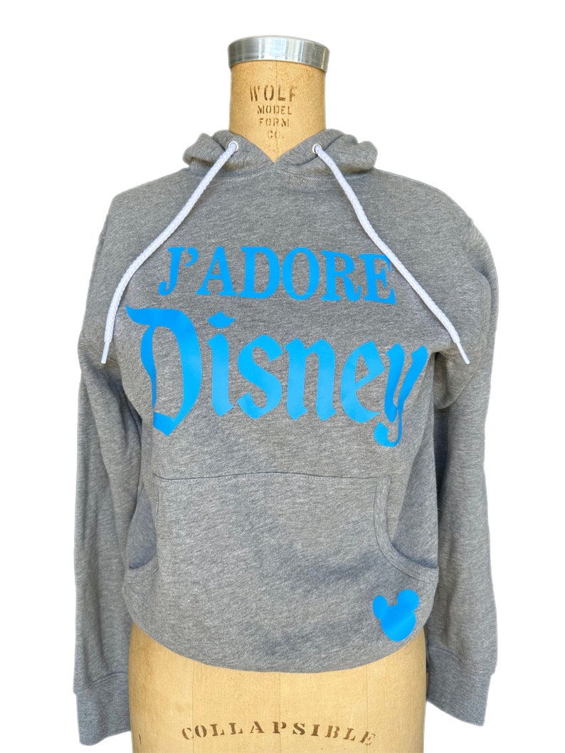 May include: Gray hooded sweatshirt with a blue graphic that says "J'ADORE DISNEY" and a blue Mickey Mouse silhouette on the pocket.