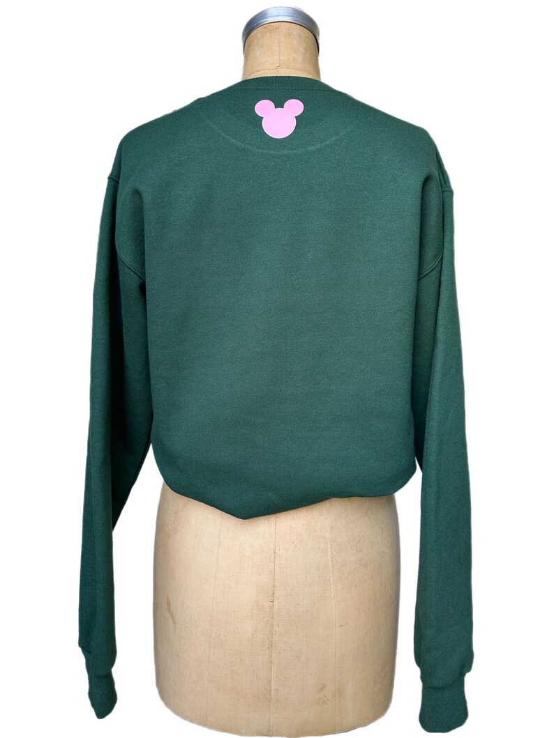 Op de afbeelding: Een donkergroen sweatshirt met lange mouwen en een roze Mickey Mouse-silhouet op de rug.