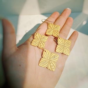 May include: Gold tone earrings with a geometric flower design. Each earring has three flower-shaped charms.