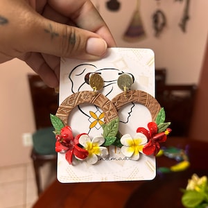 May include: A pair of brown and gold hoop earrings with red and white flower accents. The earrings are handmade and feature a geometric pattern.