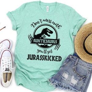 May include: A turquoise t-shirt with a black graphic that says "Don't mess with Auntie-saurus you'll get Jurasskicked". The graphic features a black silhouette of a dinosaur in a circle with claw marks around it.