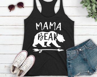 May include: Black racerback tank top with the words "MAMA BEAR" and a bear graphic in white. The tank top is paired with denim shorts, white sneakers, and sunglasses.
