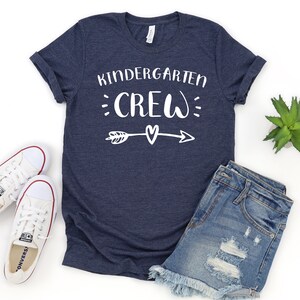 May include: A navy blue t-shirt with the text "Kindergarten Crew" in white with a white arrow and heart design.