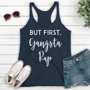 May include: A navy blue tank top with the text "BUT FIRST, Gangsta Rap" in white lettering.