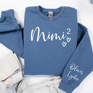 May include: A blue sweatshirt with the text "Mimi²" and two white hearts on the front. The left sleeve has the names "Oliver" and "Lydia" written in white.