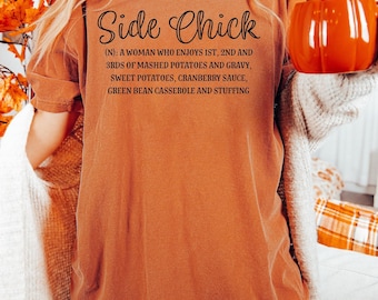 May include: A burnt orange short-sleeve t-shirt featuring black text that reads Side Chick (N): A woman who enjoys 1st, 2nd and 3rds of mashed potatoes and gravy, sweet potatoes, cranberry sauce, green bean casserole and stuffing.