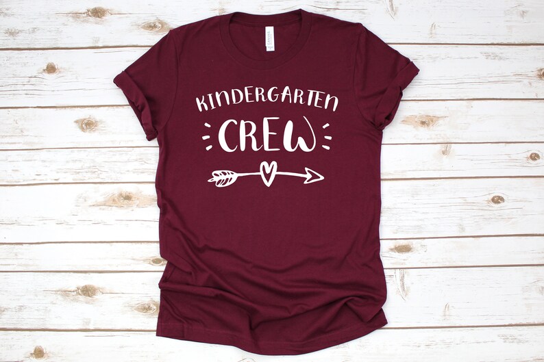 May include: Burgundy t-shirt with white text that reads "Kindergarten Crew" with a small heart and arrow graphic.