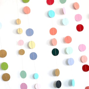 May include: A garland of colourful paper circles strung on a white background. The circles are in various shades of blue, green, yellow, pink, and red.