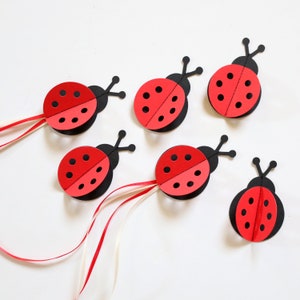 May include: Six red and black paper ladybugs with black spots. The ladybugs are cut out and have wings that fold up. They are all facing the same direction.