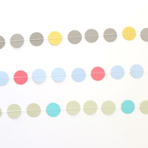 May include: A colorful garland featuring rows of circular paper cutouts in various pastel colors, including gray, yellow, pink, blue, and green. The circles are strung together with a thin, white string, creating a decorative banner.