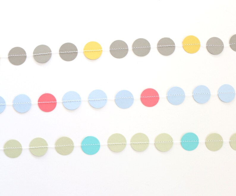May include: A colorful garland featuring rows of circular paper cutouts in various pastel colors, including gray, yellow, pink, blue, and green. The circles are strung together with a thin, white string, creating a decorative banner.