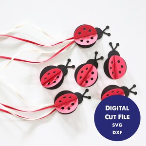以下が含まれることがあります： デジタルダウンロード用の赤と黒のテントウムシのカットファイル5つ。ファイルはSVGとDXF形式です。画像は、赤と白のリボンがついた白い表面にカットファイルが置かれている様子を示しています。