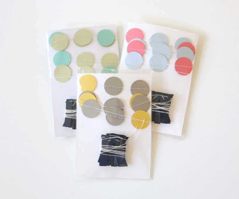 May include: Three packages of colorful paper garlands. Each garland features round paper cutouts in various pastel colors, strung together with white thread. Bundles of dark blue paper fringe are included.