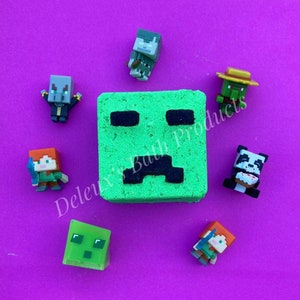 May include: A green, square bath bomb with a black Creeper face design, surrounded by small Minecraft character figurines on a purple background. The text "Deleux's Bath Products" is visible. The figurines include a panda, Alex, and a slime.