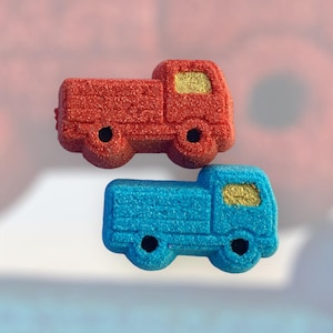 May include: Two toy trucks, one red and one blue, with gold accents. The trucks are made of a textured material and have a simple design.