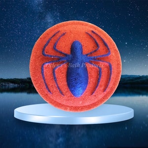 May include: A circular, orange bath bomb featuring a blue spider design. The bath bomb sits on a white plinth, set against a backdrop of a starry night sky and water. The text "Deleux's Bath Products" is visible.