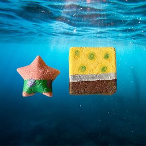 May include: Two bath bombs shaped like characters from the cartoon Spongebob Squarepants. The bath bomb on the left is a pink starfish with green pants. The bath bomb on the right is a yellow square with brown and silver accents.
