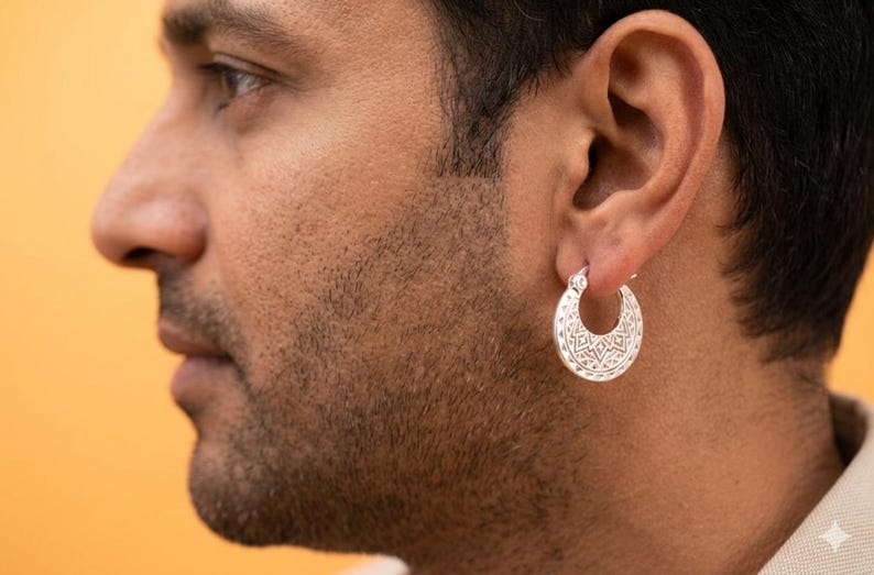 Peut inclure: Une cr&eacute;ole en argent orn&eacute;e d'un motif g&eacute;om&eacute;trique complexe et d&eacute;taill&eacute; grav&eacute; sur toute sa surface. La boucle d'oreille est de forme circulaire avec une finition m&eacute;tallique polie, pr&eacute;sentant un design sym&eacute;trique r&eacute;p&eacute;t&eacute; sur la face externe.
