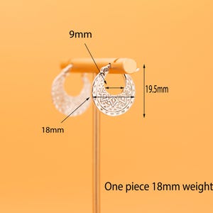 Peut inclure: Une paire de cr&eacute;oles argent&eacute;es avec un motif g&eacute;om&eacute;trique d&eacute;coup&eacute;. Les boucles d'oreilles mesurent 18 mm de largeur, 19,5 mm de hauteur, avec un diam&egrave;tre int&eacute;rieur de 9 mm. Chaque boucle p&egrave;se 2,1 grammes, comme indiqu&eacute; par le texte.