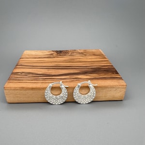 Peut inclure: Une paire de cr&eacute;oles en argent pr&eacute;sentant un motif g&eacute;om&eacute;trique textur&eacute; sur la moiti&eacute; inf&eacute;rieure de l'anneau circulaire. Les boucles d'oreilles sont dot&eacute;es d'un m&eacute;canisme de fermeture &agrave; charni&egrave;re et d'une finition mate avec des gravures.