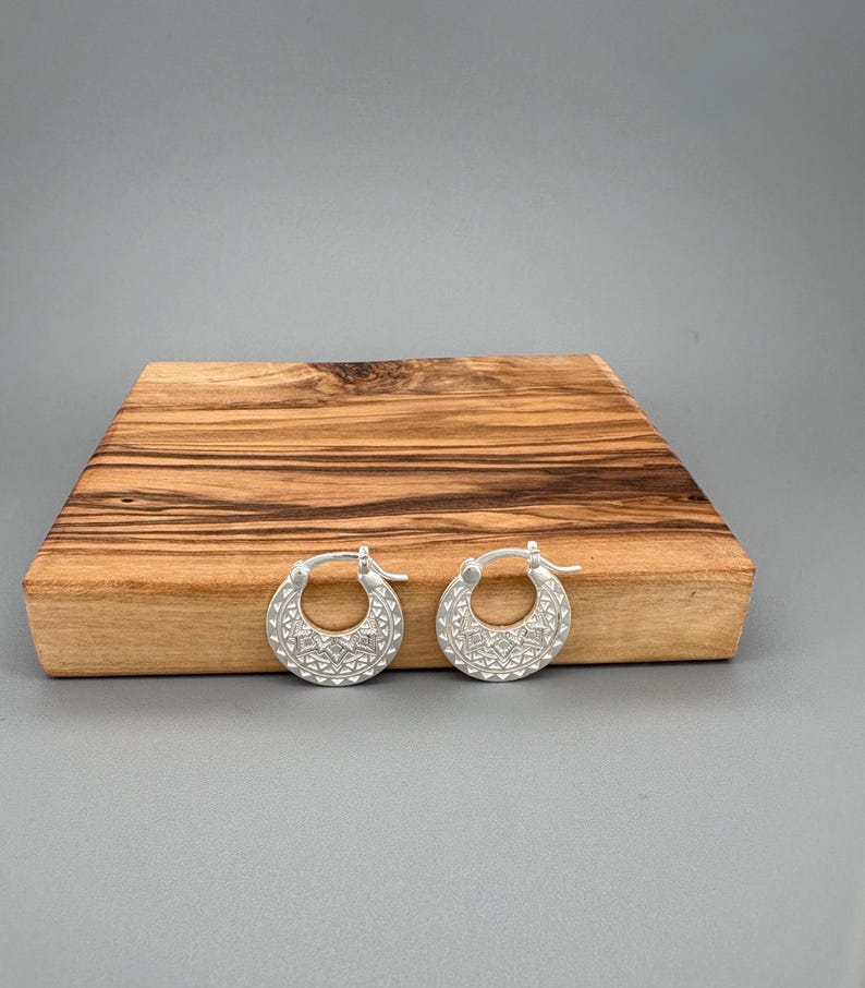 Peut inclure: Une paire de cr&eacute;oles en argent pr&eacute;sentant un motif g&eacute;om&eacute;trique textur&eacute; sur la moiti&eacute; inf&eacute;rieure de l'anneau circulaire. Les boucles d'oreilles sont dot&eacute;es d'un m&eacute;canisme de fermeture &agrave; charni&egrave;re et d'une finition mate avec des gravures.
