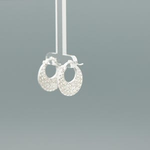Peut inclure: Une paire de petites cr&eacute;oles en argent pr&eacute;sentant un motif g&eacute;om&eacute;trique textur&eacute; et d&eacute;taill&eacute; sur la surface ext&eacute;rieure. Les boucles d'oreilles sont de forme circulaire avec un m&eacute;canisme de fermeture &agrave; charni&egrave;re et une finition m&eacute;tallique brillante.