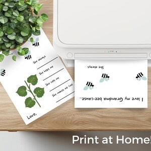 May include: Two white sheets of paper with bee graphics and text are on a wooden surface. One sheet has fill-in-the-blank lines and a leafy vine illustration. The other sheet is printing from a white printer. The text "Print at Home!" is at the bottom.