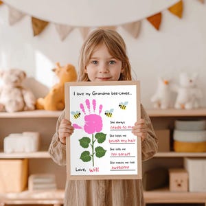 May include: A child holds a framed print with the text "I love my Grandma bee-cause..." and a pink handprint flower design. The print includes the phrases "She always reads to me," "brush my hair," "I'm smart," and "awesome."